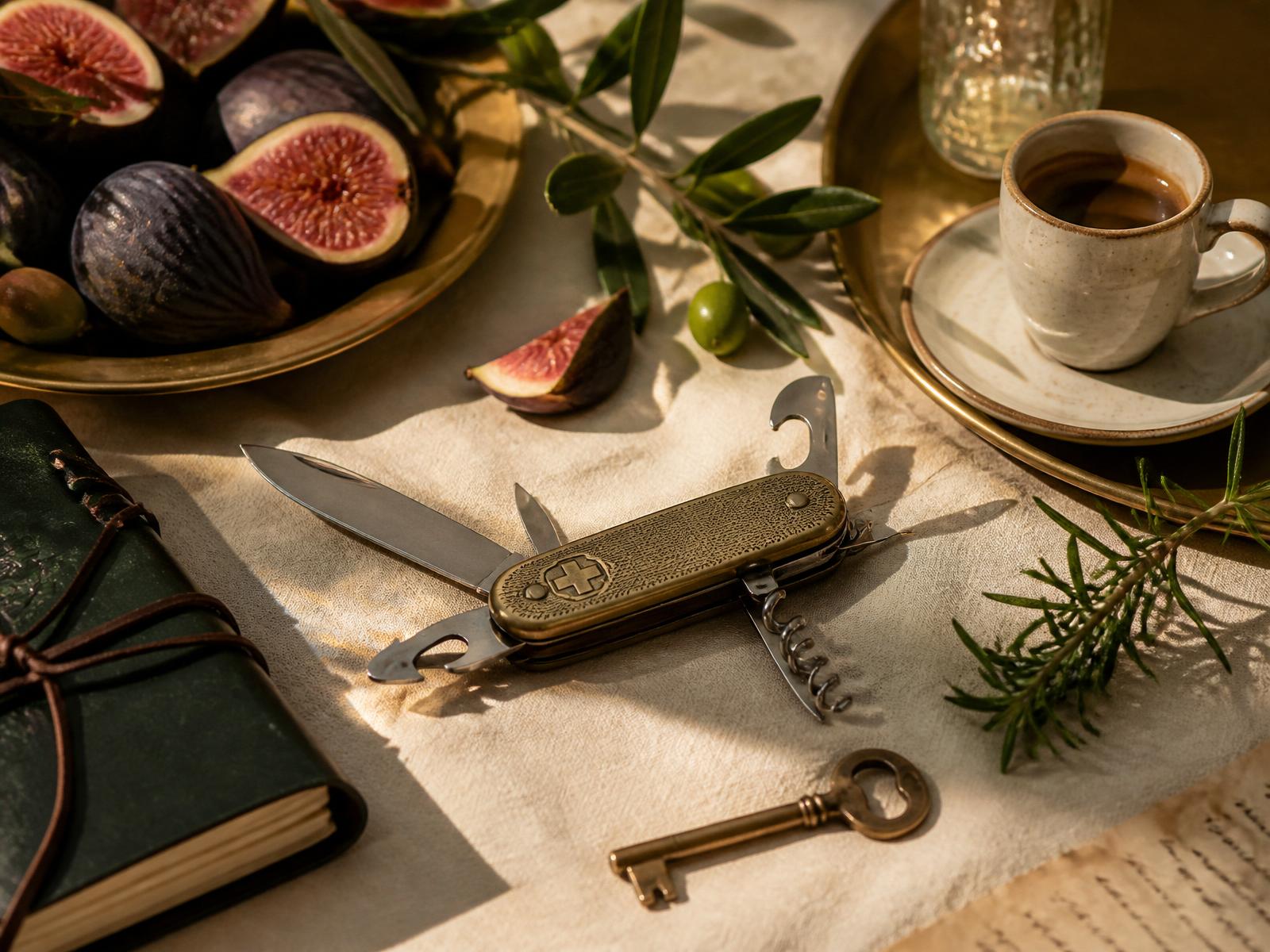 A brass Swiss army knife on warm linen, surrounded by figs, olive branches and a leather journal